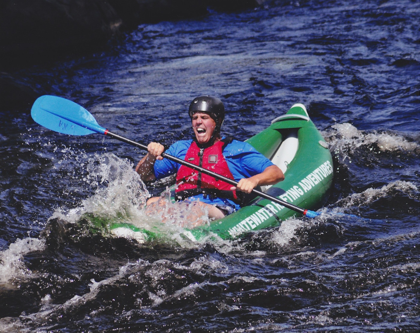 Person rafting in a green inflatable kayak on a turbulent river.