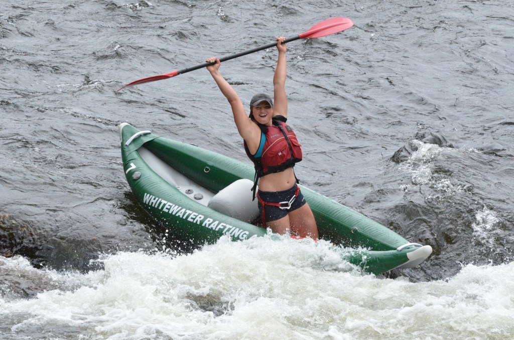 Person in kayak raises paddle triumphantly on a river.