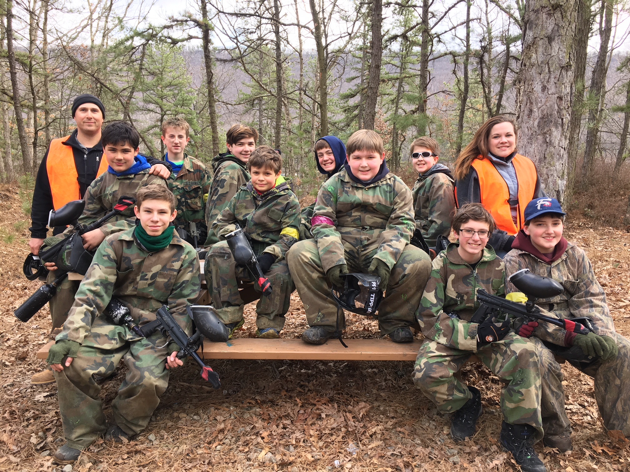 Group of youth in camouflage holding paintball guns in a wooded area.