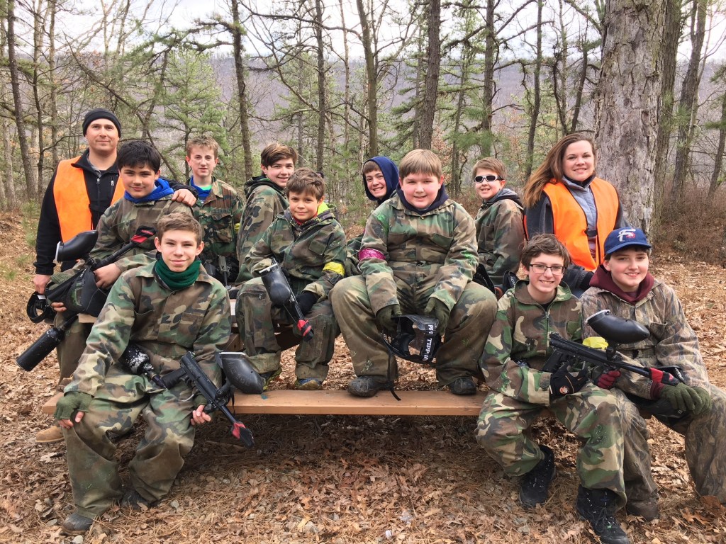 Group of youth in camouflage holding paintball guns in a wooded area.