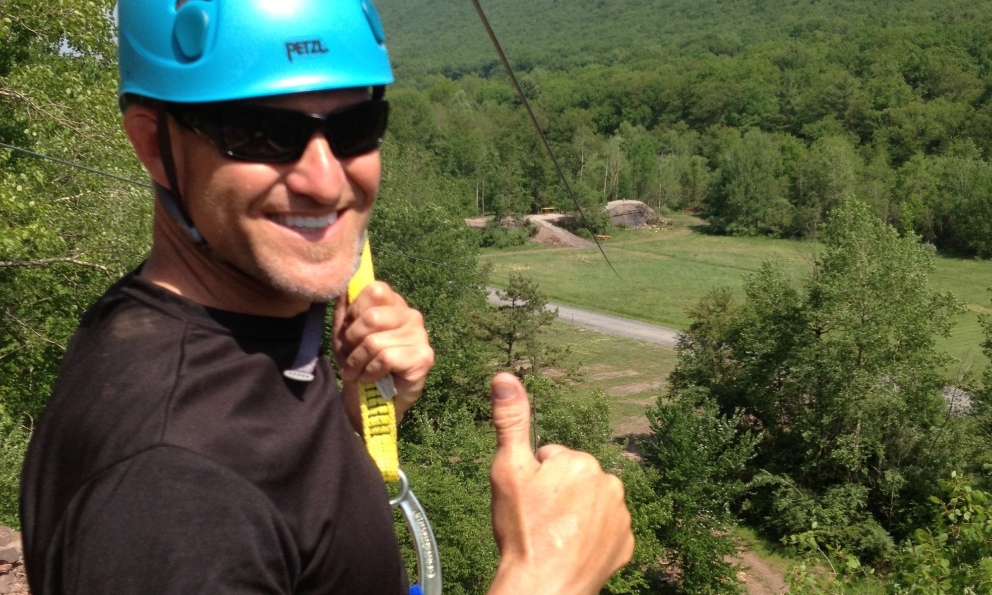 Man giving thumbs up while zip-lining over a forest.
