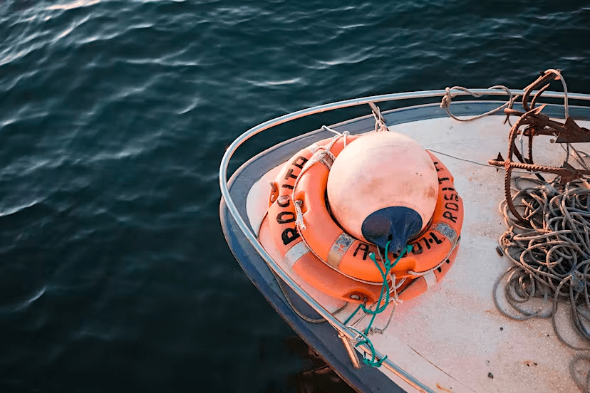 Boat bow with lifebuoy, buoy, and ropes on water.