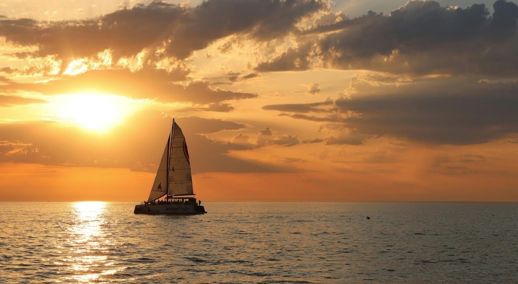 Sailboat on calm sea during sunset with cloudy sky.