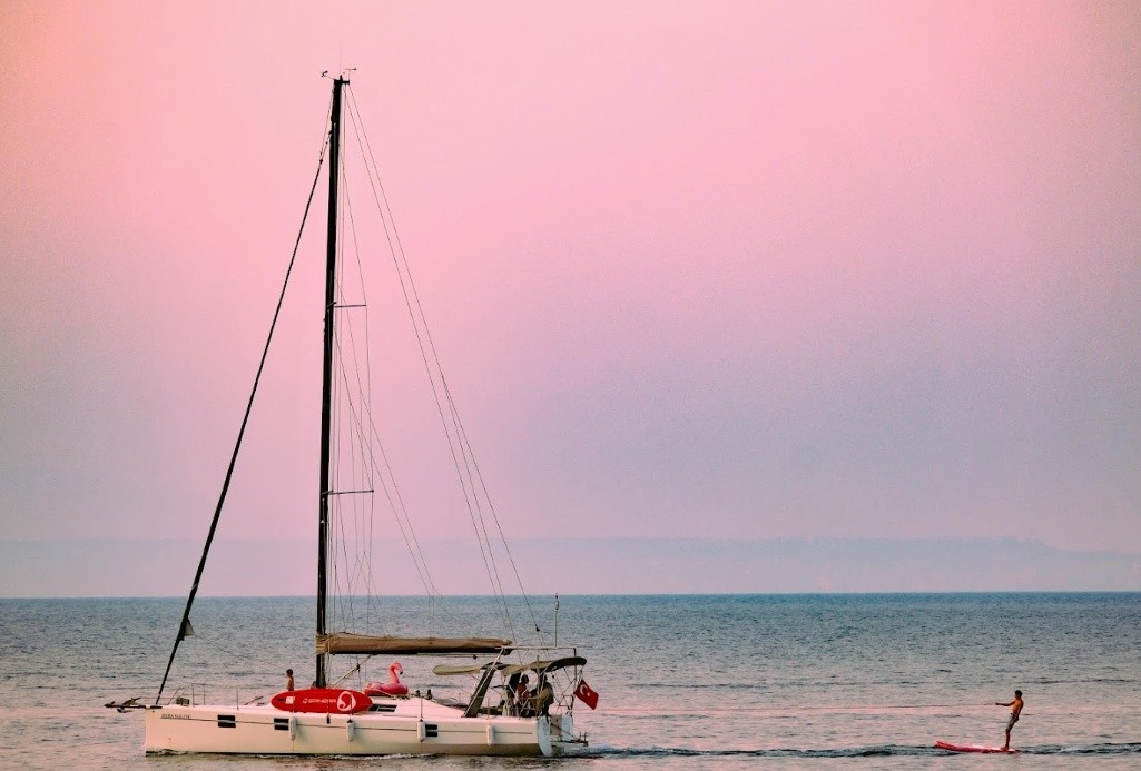 Sailboat and paddleboarder on calm sea at pink sunset.