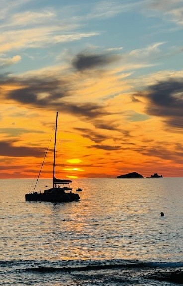 Sailboat silhouette on calm ocean water at sunset.
