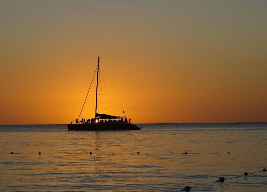 Silhouette of a sailboat at sunset on calm water.