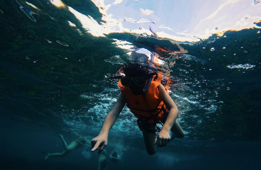 Person snorkeling underwater wearing an orange life vest and goggles.