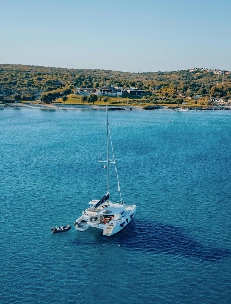 Catamaran on blue water near green coastline under clear sky.