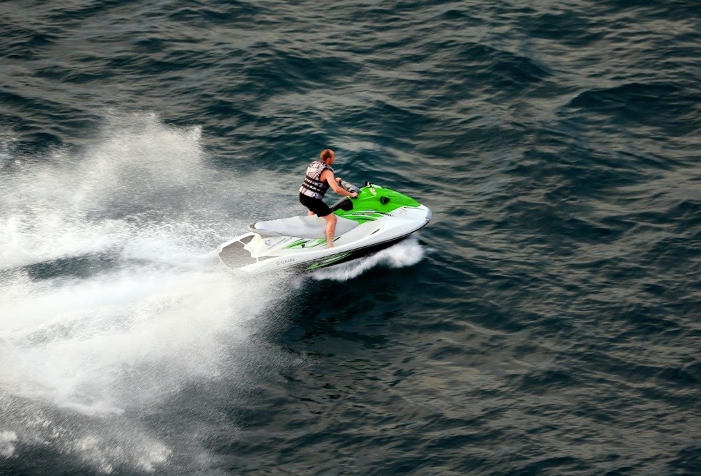 Person riding a green and white jet ski on open water, creating a large spray.