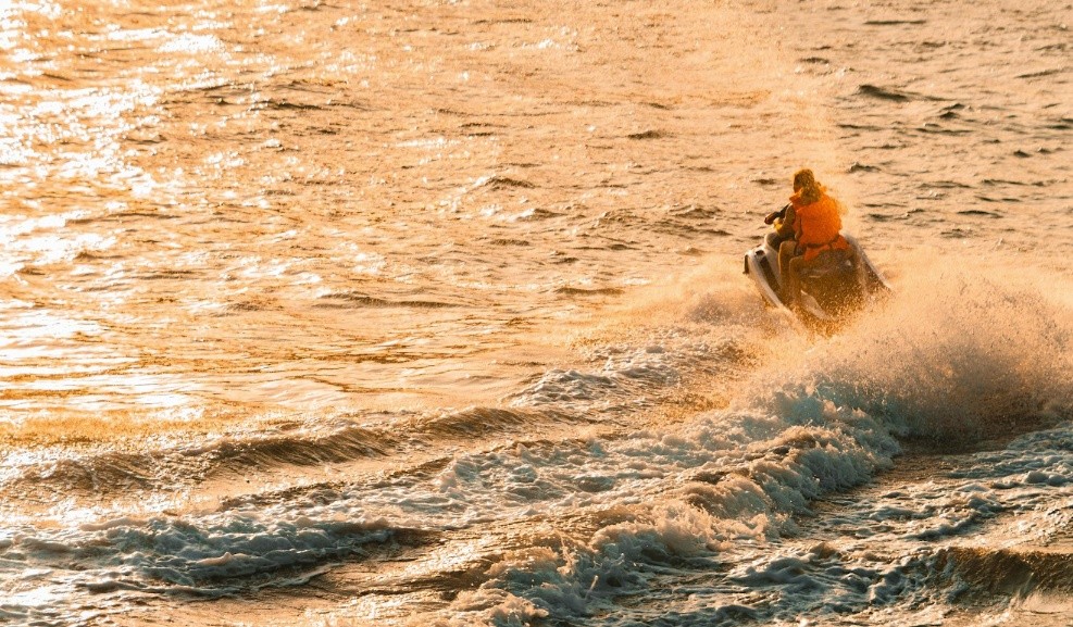 Person on jet ski rides through waves during a golden sunset.