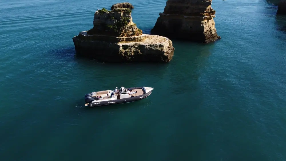 A motorboat near large rocks in calm blue water.