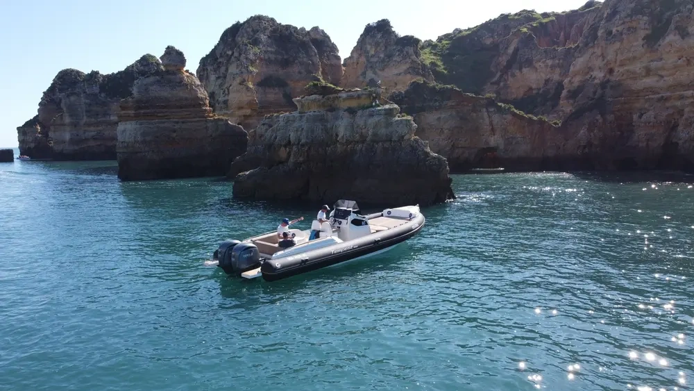 Boat near rocky cliffs in clear blue water on a sunny day.