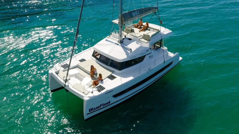 White catamaran with people sunbathing on turquoise water.