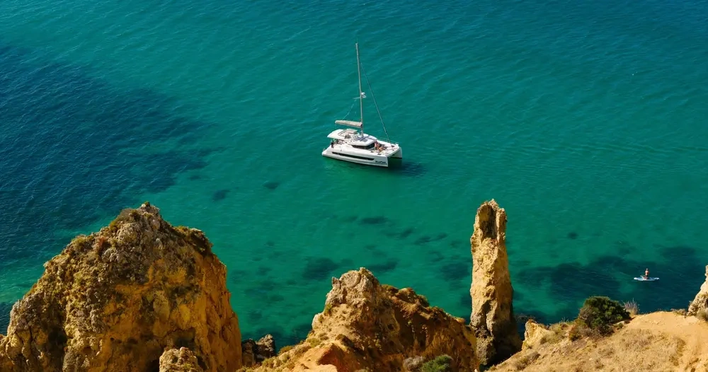 Sailboat on turquoise sea near rocky cliffs.