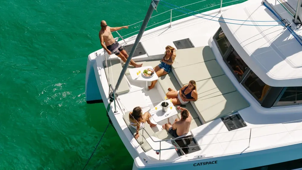 Five people relaxing on a catamaran yacht in clear turquoise water.