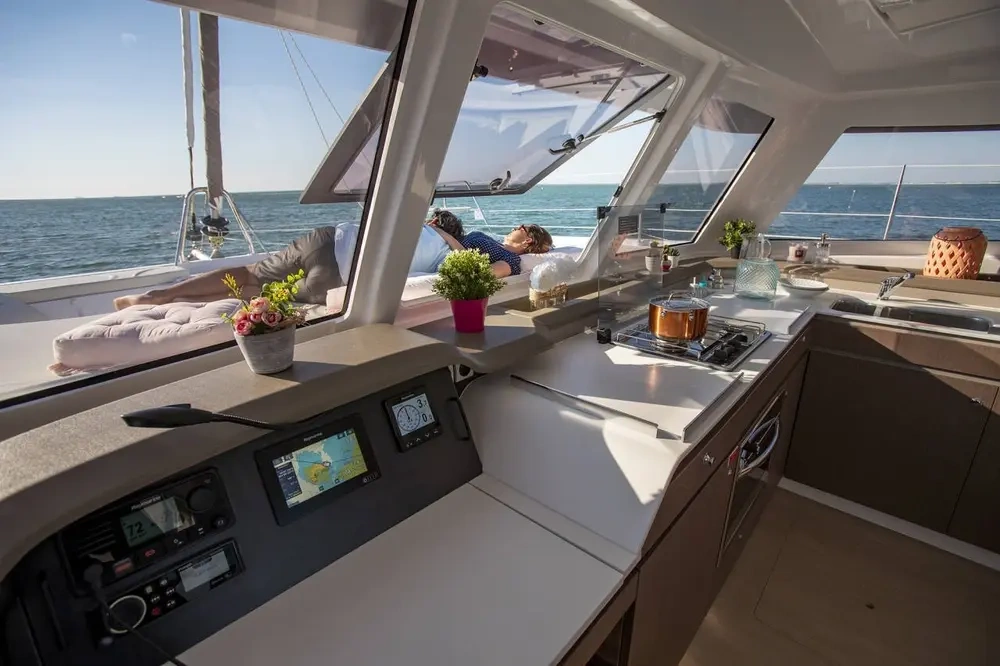 View from catamaran's kitchen with person relaxing outside on deck.