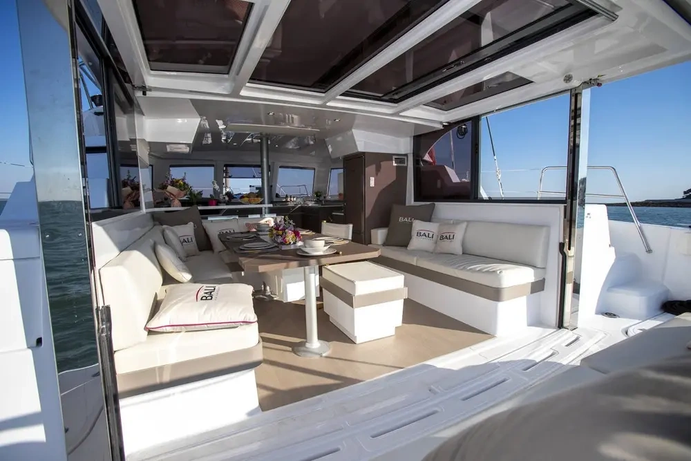 Open deck of a yacht with seating area and table, overlooking the sea.