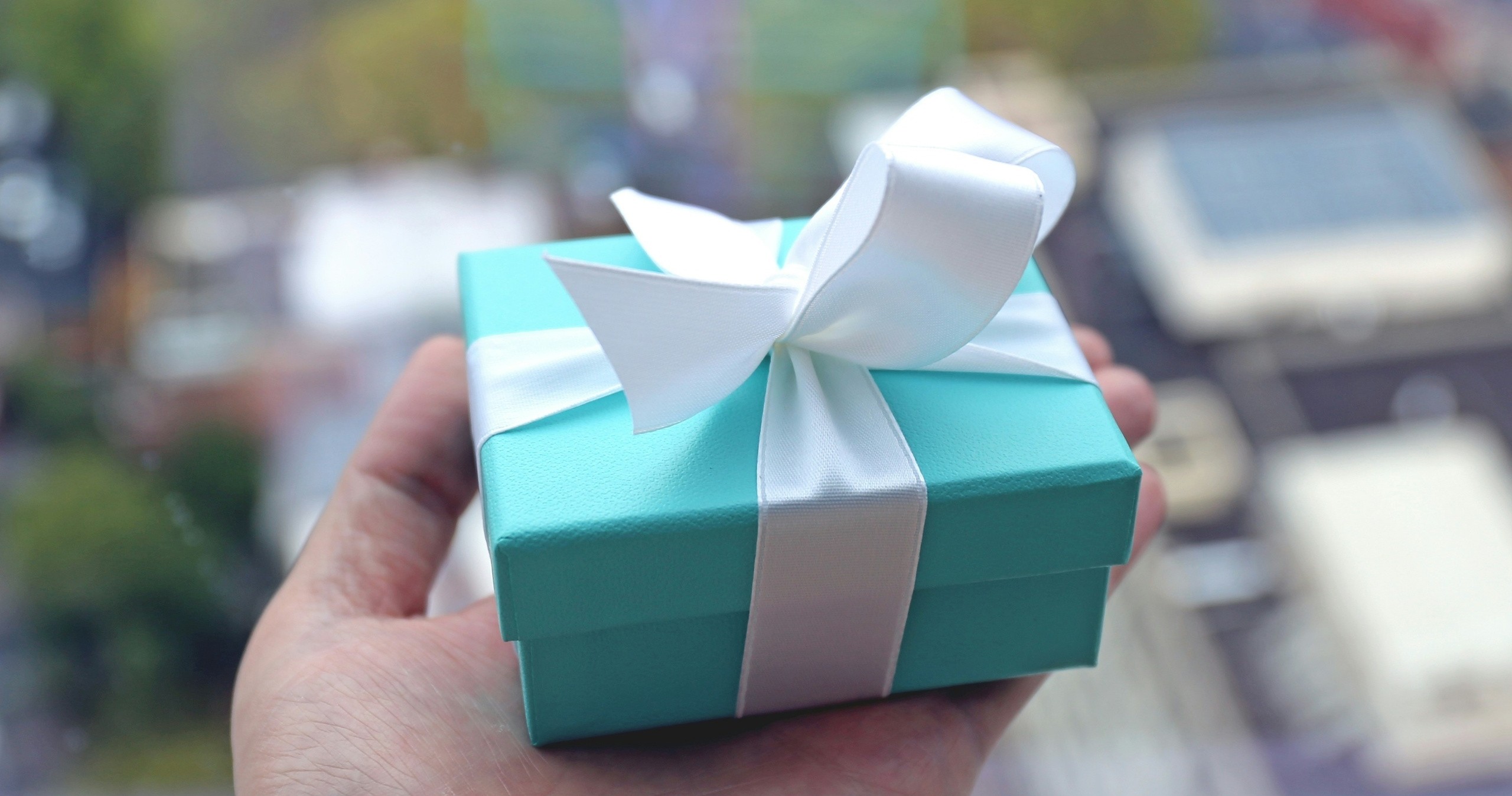 Hand holding a small turquoise gift box with white ribbon.