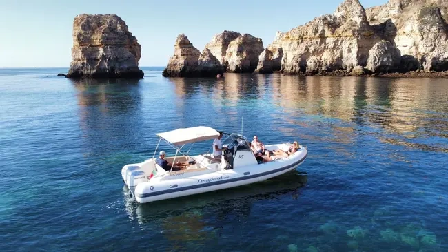 Motorboat with people near rocky cliffs on calm, blue water.