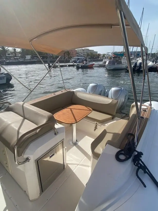 Small boat deck with seating, table, and canopy, docked in marina.