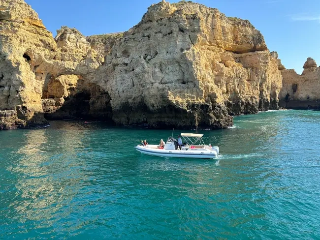 A small boat with people on blue water near large rocky cliffs.