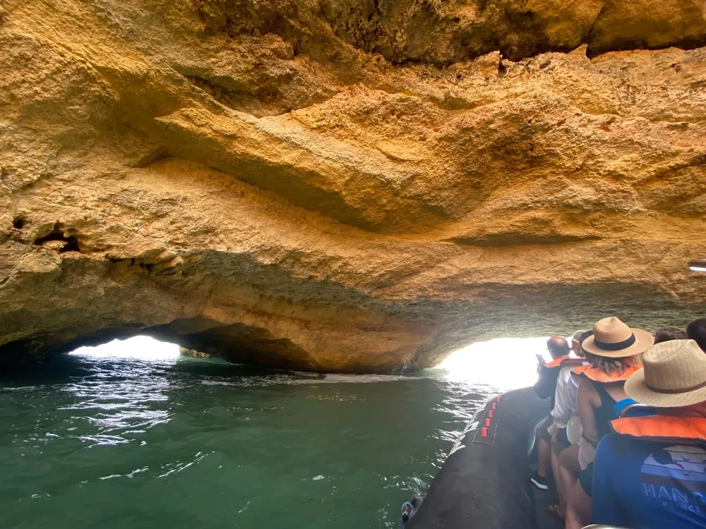 People in a boat exploring a rocky cave on a sunny day.