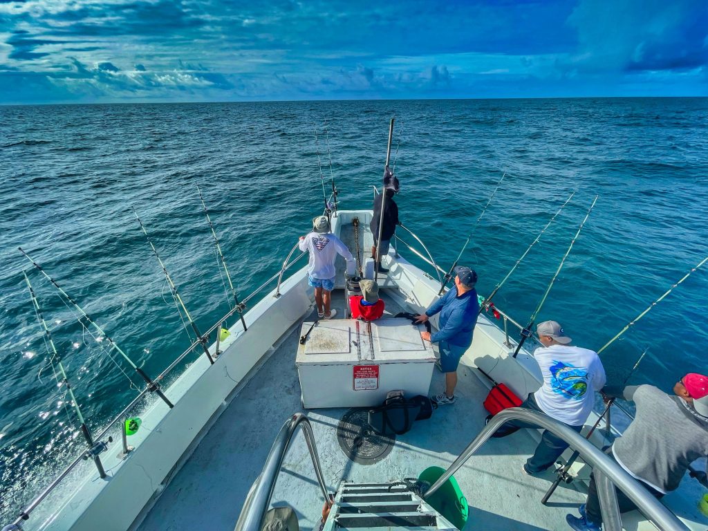 People fishing on a boat in open ocean under a partly cloudy sky.