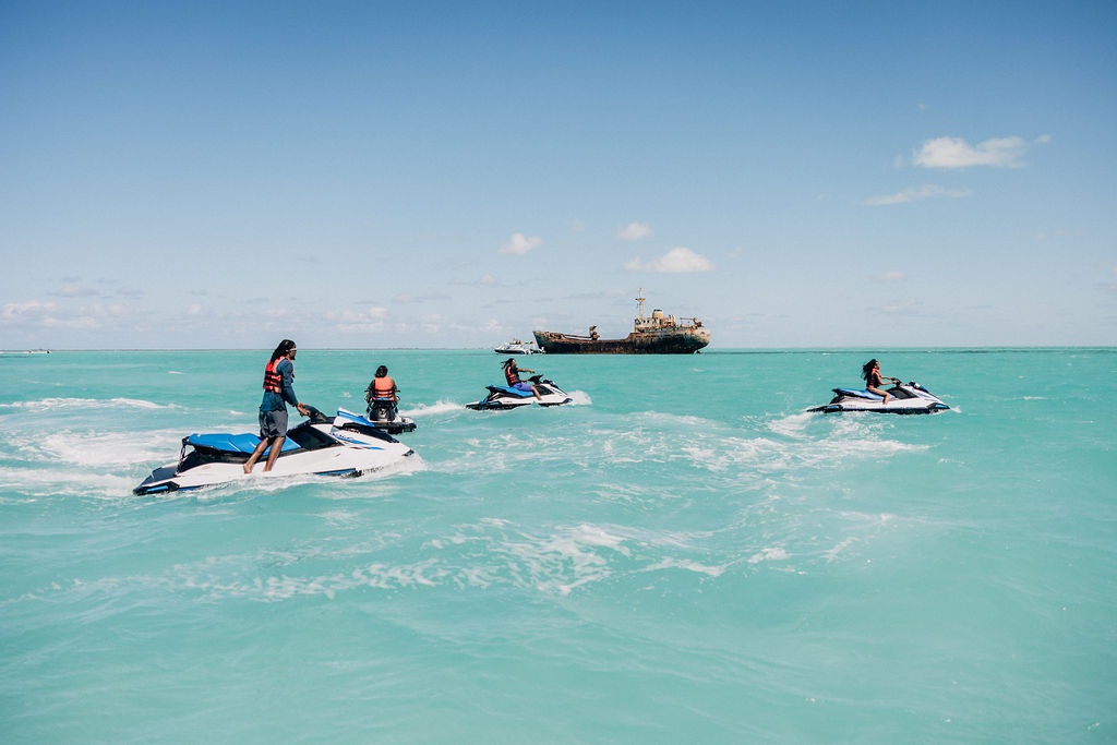 Four people on jet skis in turquoise sea with a distant ship.