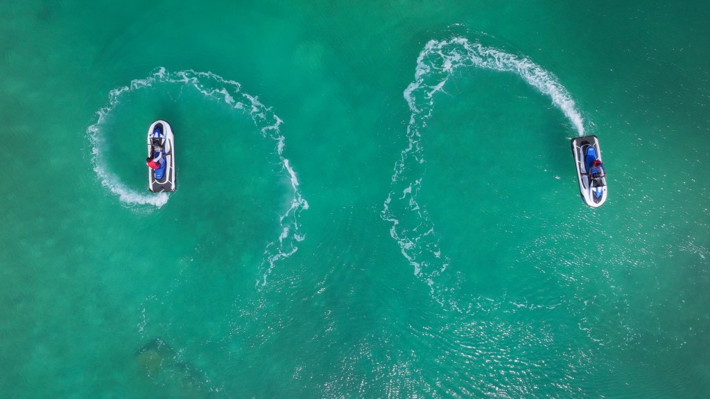Two jet skis leaving curved trails on turquoise water.
