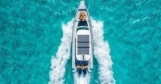 Aerial view of a boat with people on turquoise water creating waves.