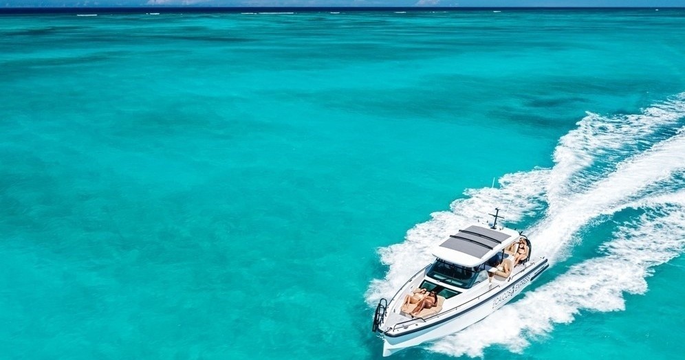 White boat speeding on turquoise ocean with wake trails under clear blue sky.