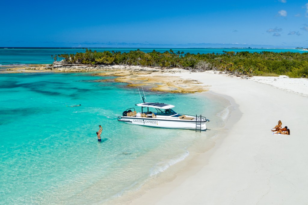 White sandy beach with turquoise water, a boat, and two people relaxing.