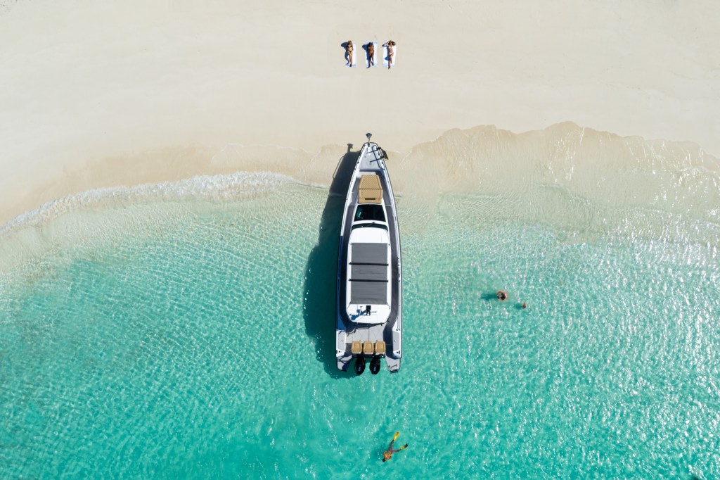 Aerial view of a boat on a beach with people sunbathing and swimming in clear water.