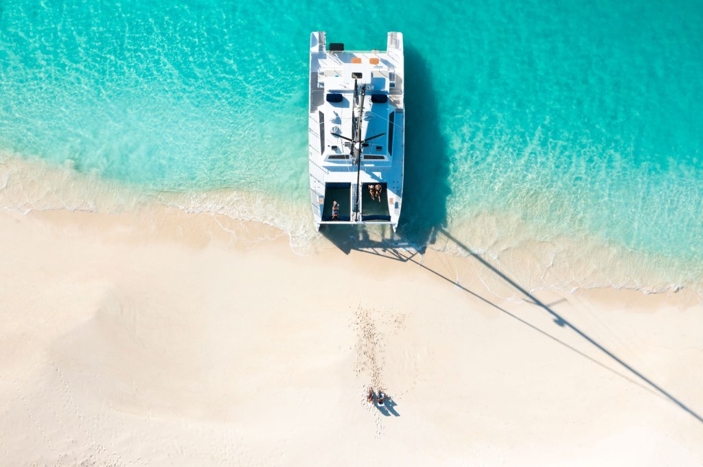 Aerial view of a catamaran on a sandy beach with turquoise water.