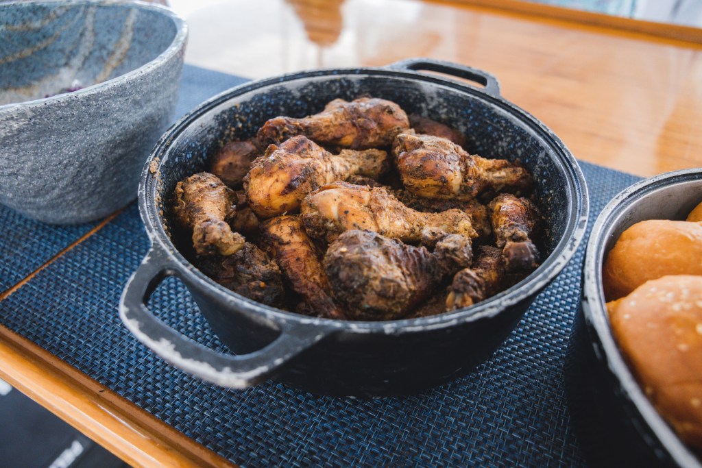 Cooked chicken pieces in a black pot on a blue mat with a bowl nearby.
