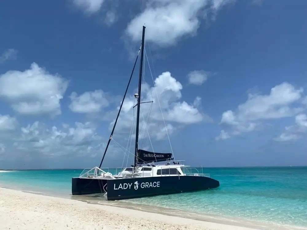 Catamaran named 'Lady Grace' on a sandy beach by turquoise sea under a partly cloudy sky.