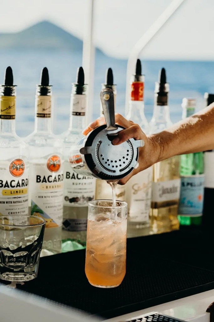 Bartender pouring drink from shaker with liquor bottles in background.