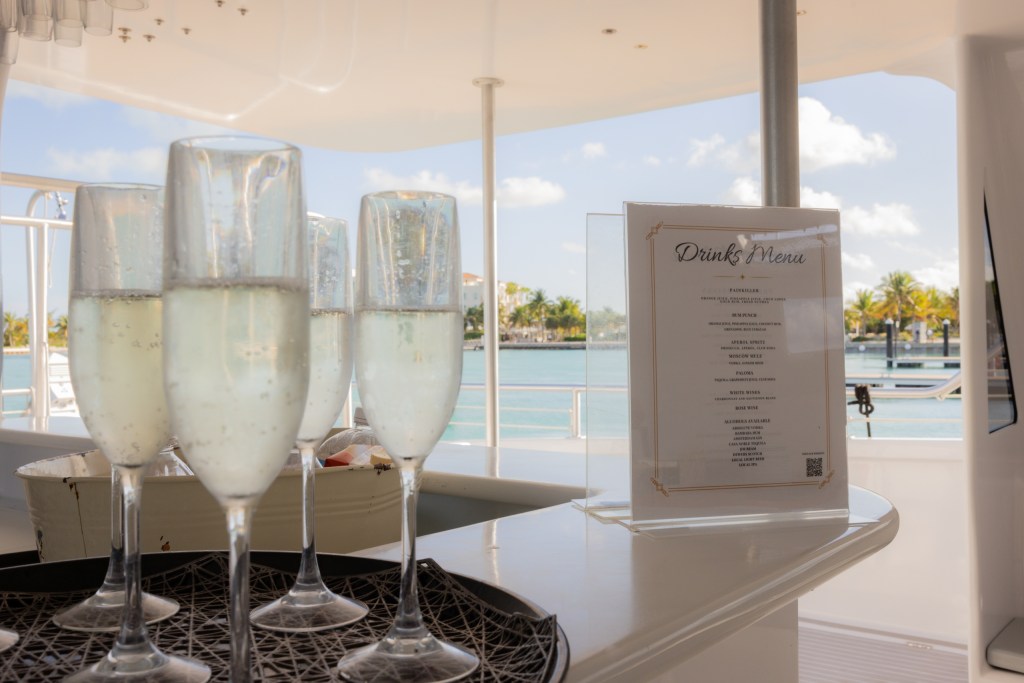 Tray of champagne glasses and drink menu on a boat deck with water view.