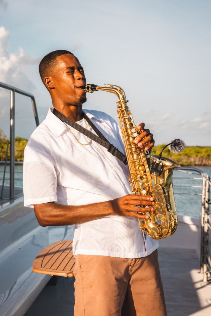 Man playing saxophone on a boat, sunny day.