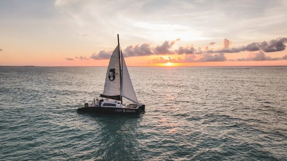 Sailboat on ocean at sunset with a distant horizon and clouds.