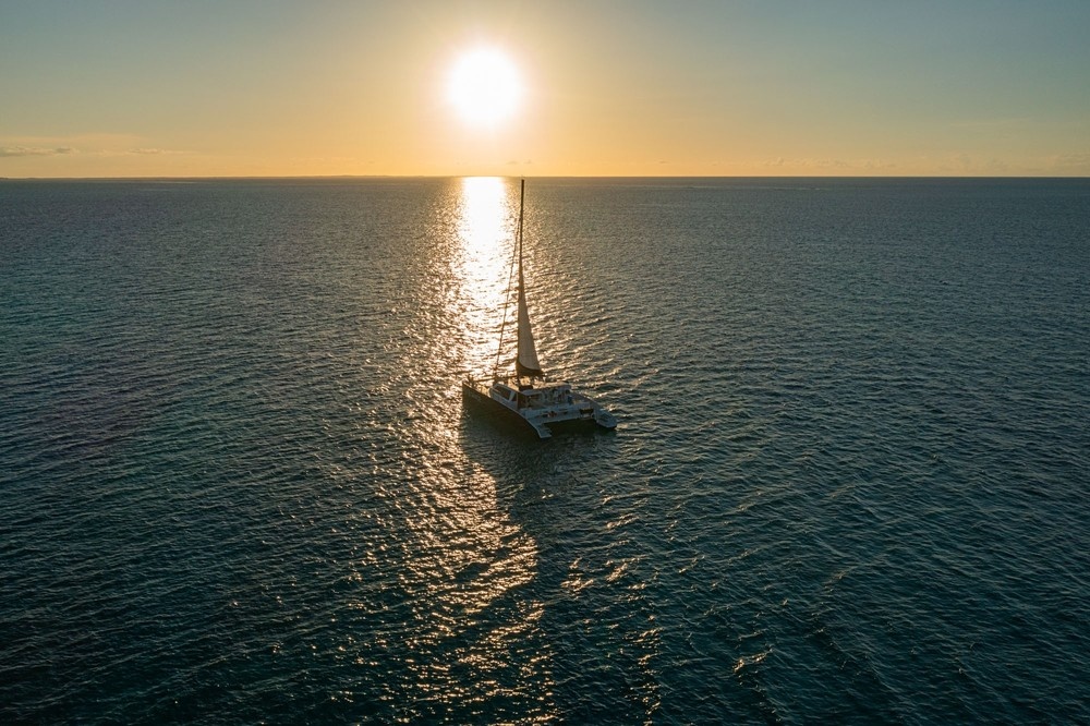 Sailboat on ocean at sunset with sun reflecting on water.