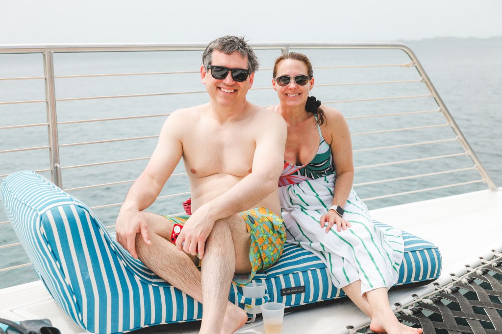 Man and woman in swimsuits sitting on a boat, smiling.