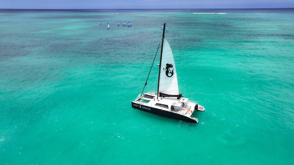 Catamaran sailing on turquoise ocean with distant boats visible.