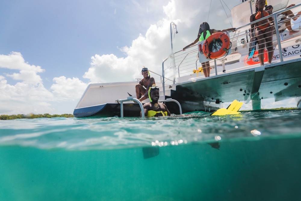 Two people snorkeling near a boat in clear blue water under a cloudy sky.