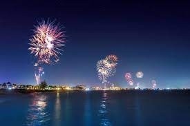 Colorful fireworks light up a night sky over a body of water.