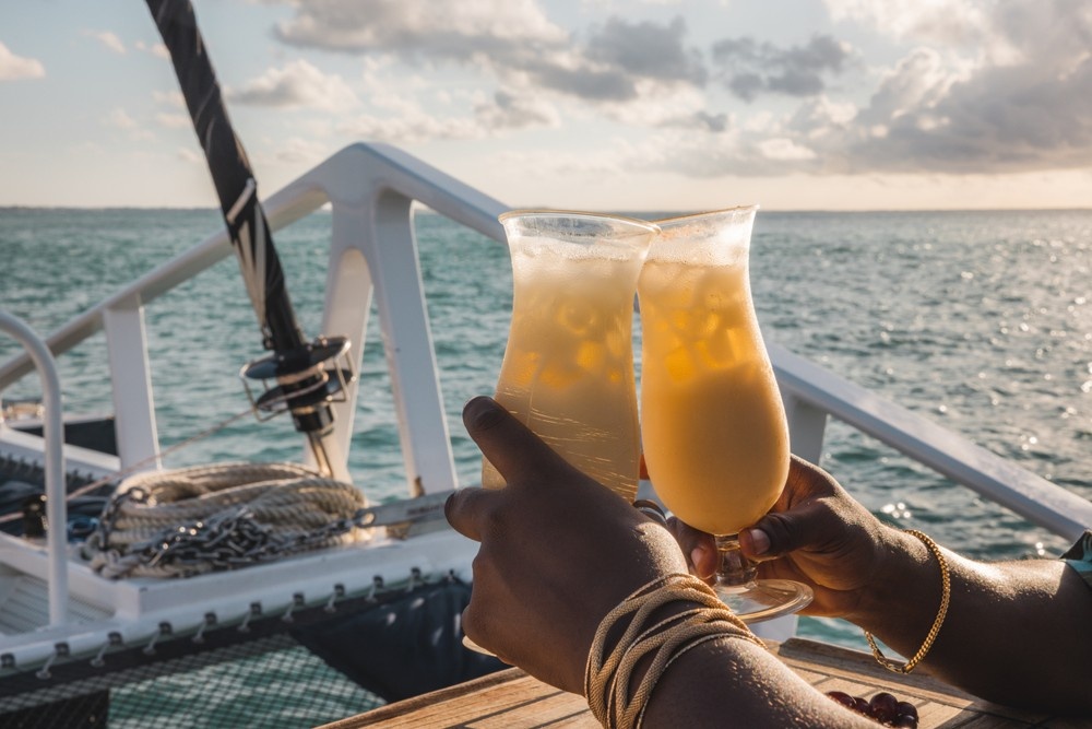 Two people toasting with tropical drinks on a boat at sunset.