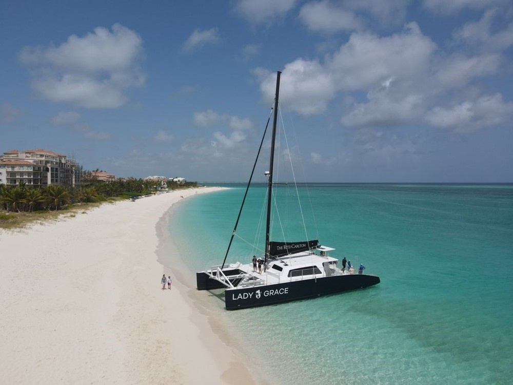 Catamaran 'Lady Grace' on a beach near turquoise sea under a partly cloudy sky.