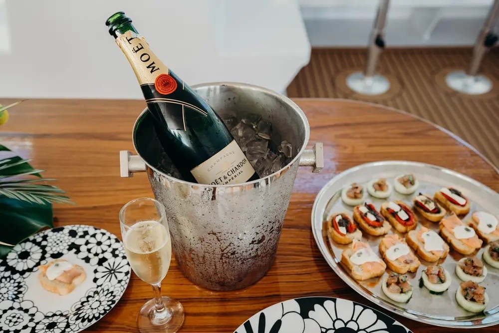 Champagne bottle in ice bucket with snacks on a tray.