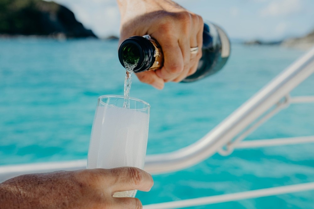 Person pouring champagne into a glass on a boat with turquoise water in the background.