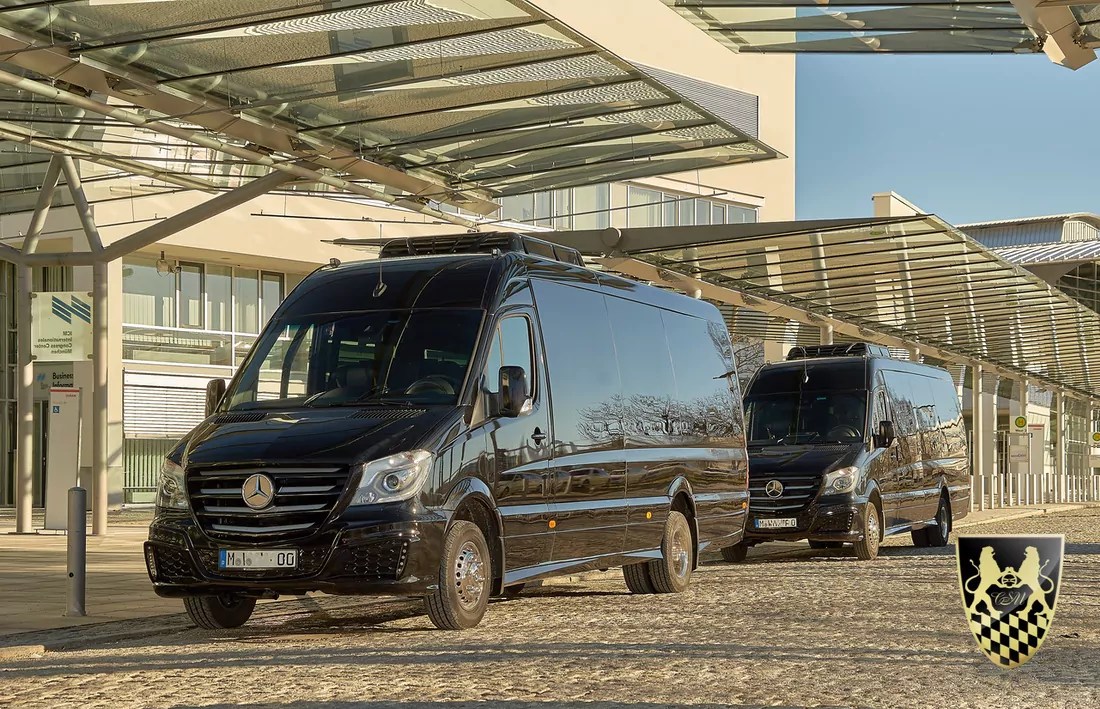 Two black Mercedes vans parked under glass canopies in a modern urban area.